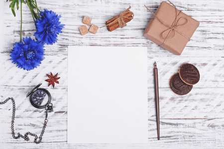 Mock up of empty paper, flower, ink pen, cakes, shuga, anise and gift on white wood desk. Flat Lay...