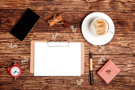 a cup of coffee, notebook, ink pen, phone and wooden words Love on wooden backgroundの写真素材
