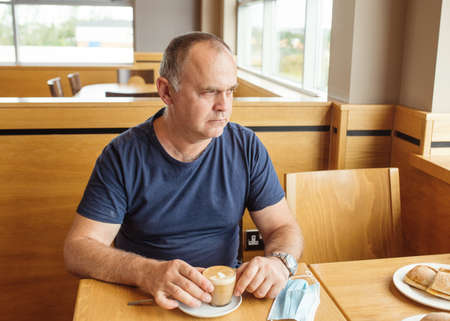 The man removing the mask and drinking coffee in the cafe during lockdownの写真素材