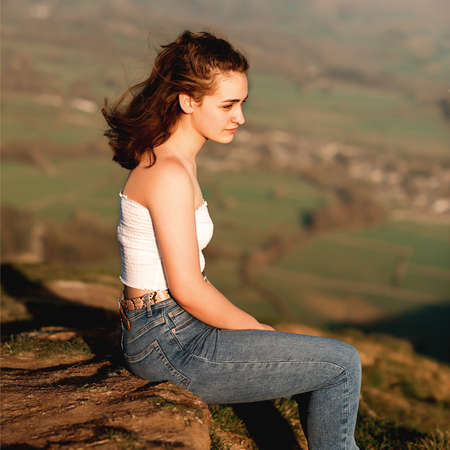 A girl sitting on top of the hill against amazing landscape in the summerの写真素材