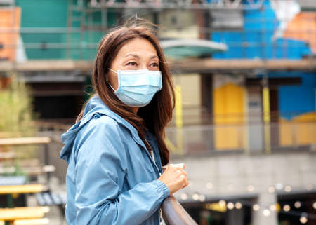 Asian woman in a face mask and a blue coat walking around Europe cityの写真素材