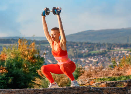 woman doing dumbbell exercises in the park against cityの写真素材