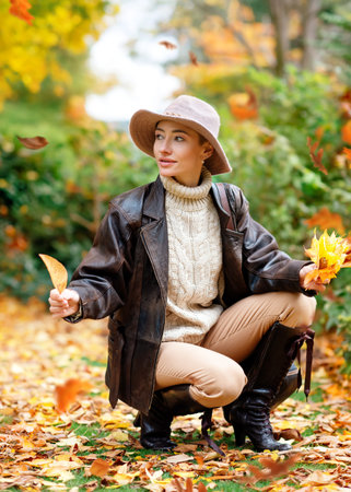 woman in hat  sitting on the autumn leaves in the park