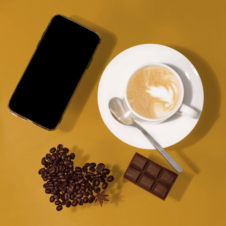 cup of coffee with chocolate, heart shape beans, phone on a tableの写真素材