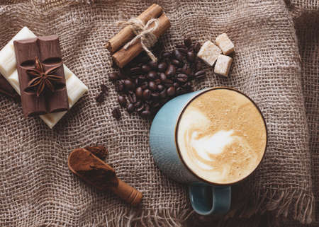 big cup of coffee with cinnamon, anise, coffee beans, chocolate on wooden background view aboveの写真素材