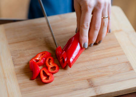 Woman cooking salad and cutting pepper on chop board in a kitchenの写真素材