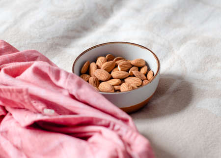 white bowl with peanuts and almond on a bedの写真素材