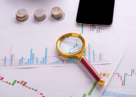 phone, coins, magnifying glass on chartの写真素材