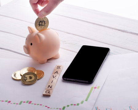 person putting gold bitcoin in piggy bank on a desk and others bitcoins, phone, schedules and title...