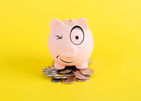 smiling piggy bank on Pile of coins  on yellow backgroundの写真素材