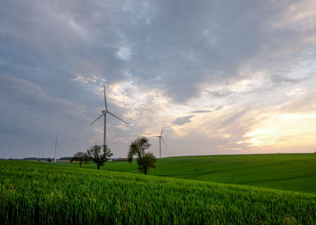 An electricity generating windmills on the green field against cloudy blue sky in Englandの写真素材
