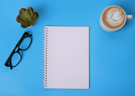 notebook, glasses, cup of coffee and plant on blue backgroundの写真素材