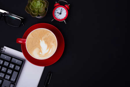 red cup of coffee, pen, glasses, alarm,  plant, phone, paper on black background  top viewの写真素材
