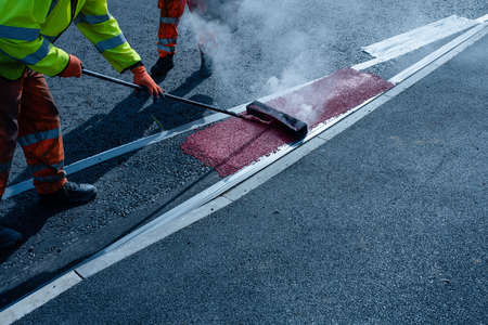 Roadworker applying thermoplastic road marking on the freshly laid tarmac during new roundabout and road constructionの写真素材