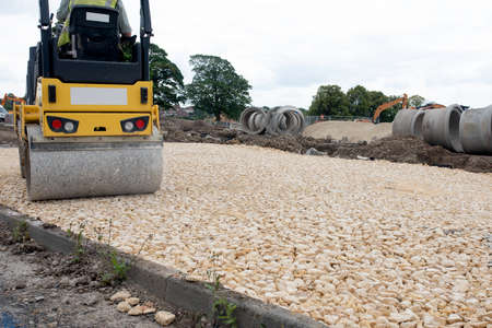 Road roller compacting stone during new road construction in preparation for tarmac, on housing development siteの写真素材