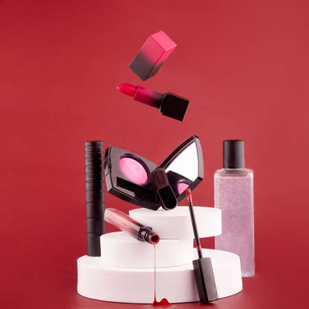 lipstick, lip gloss, mascara, eye shadow, blush on props on a red background. concept cosmetics for flyersの写真素材