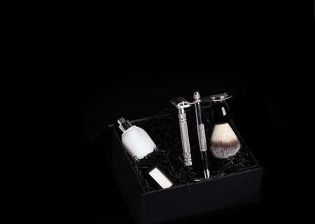 Razor and brush on stand, perfume, balsam and blades in black box on a black background. Space for textの写真素材