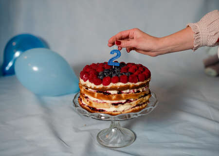 mother put candle to birthday cake on blue backgroundの写真素材