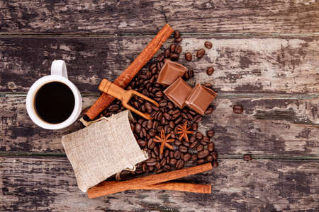 cup of coffee with chocolate, cinnamon sticks,   and coffee beans on wooden backgroundの写真素材