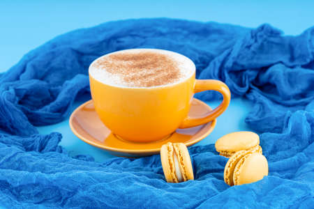 yellow cup of coffee and macaroons on blue backgroundの写真素材