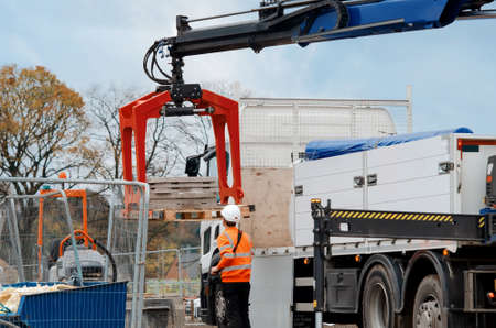 Construction materials delivered on site and being offloaded by hydraulic truck mounted craneの写真素材