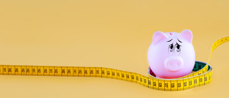 piggy bank wrapping with a centimetre on a yellow backgroundの写真素材