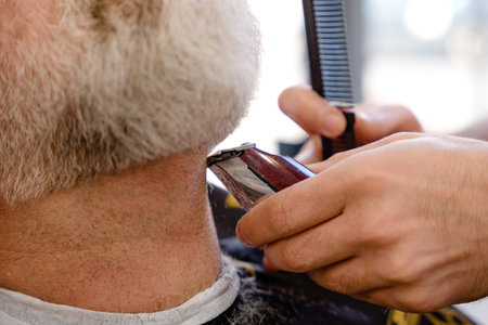 Barber trimming and cutting bearded man with shaving machine in barbershop. Hairstyling process.の写真素材