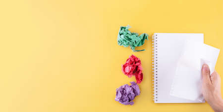 a hand tearing and  a sheet from a notebook on a yellow background. next to the colorful crumpled sheets. turning over a new leafの写真素材