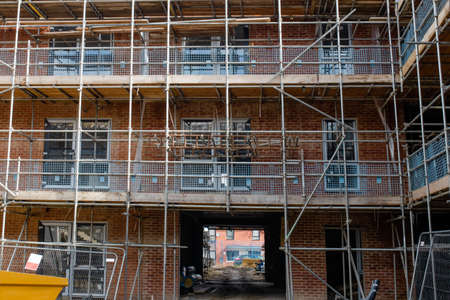 New build residential multistorey appartment building made of brick and concrete block, with scaffolds erected around it to provide access for 
external construction worksの写真素材