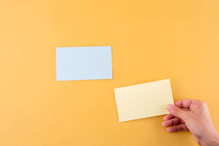 hand putting blank writing paper and empty paper on a yellow background. space for text.の写真素材