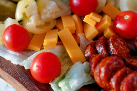 cherry tomatoes, sweet peppers,  pickled cucumbers, pickled garlic, olives,  sausage, different cheese, bacon on wooden plate. Snack foodの写真素材