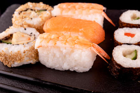 Close up of delicious japanese food with sushi rolls  with salmon, tuna,   shrimp with black chopsticks  on black backgroundの写真素材