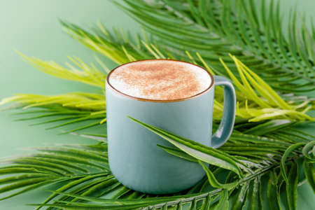 green mug of coffee on a large green leaves on a yellow backgroundの写真素材