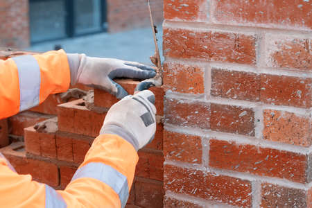 Bricklayer laying bricks on mortar on new residential house construction. Get construction qualificationの写真素材