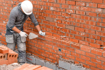 Bricklayer laying bricks on mortar on new residential house constructionの写真素材