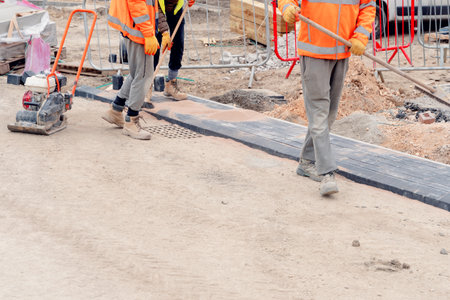 Paving stone workers filling joints of the block paved footpath with dry sand during the construction of a new roadの写真素材