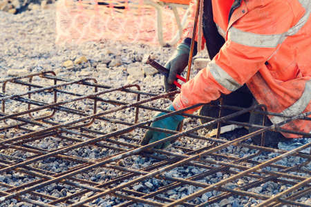 Builder's hands fixing steel reinforcement bars at construction site. Steel fixer assembling reinforcement cage. Selective focusの写真素材