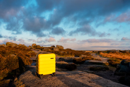 Yellow Suitcase with orange scarf on top of hill or mountain against blue sky at sunrise. Travel concept.の写真素材