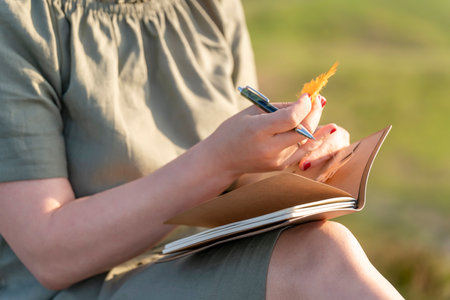 A woman holds a pen, a diary and a pen in nature. The concept of a lifestyle in travel. The concept of local tourism.の写真素材