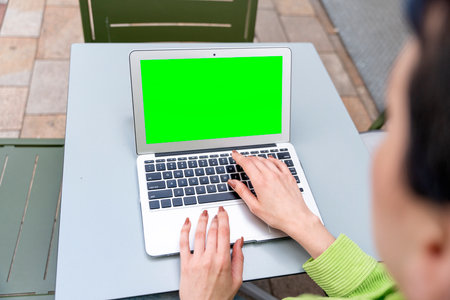 woman having coffee at the street cafe outside, talking on the laptop with green screen and having fun time. lifestyle conceptの写真素材