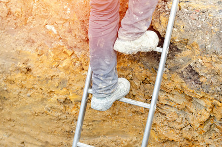 Builder going up the ladder to get out of trenchの写真素材