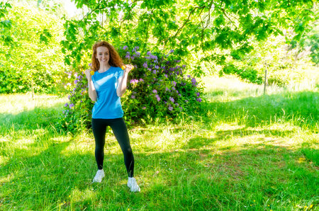 redhead woman doing fitness exercise with dumbbells outdoor in a park Fitness, sport, healthy lifestyle conceptの写真素材