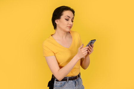 surprised woman in yellow t-shirt and jeans using a mobile phone on yellow backgroundの写真素材