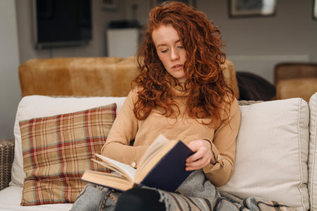 a beautiful redhead girl reading a book, concepts of home and comfortの写真素材