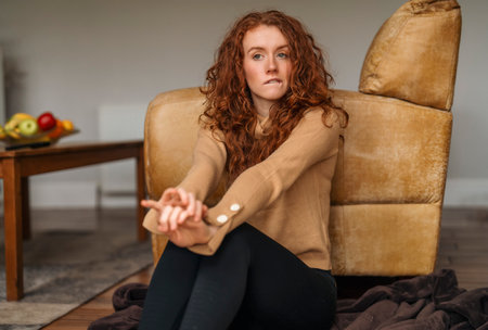 Young woman relaxing at home, sitting on floor near a sofa in living room. Beautiful natural girl stay at homeの写真素材