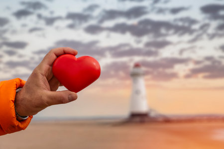 red heart in hand against lighthouse. Fall in love with holiday at seaside conceptの写真素材