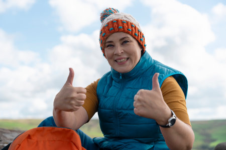 Excited Woman with thumbs up reaching destination sitting on top of mountain Travel Lifestyle conceptの写真素材