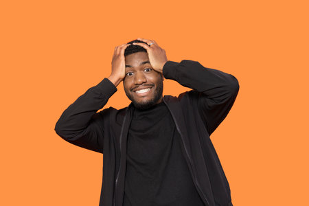 man with hand on head hearing unexpected news on orange backgroundの写真素材