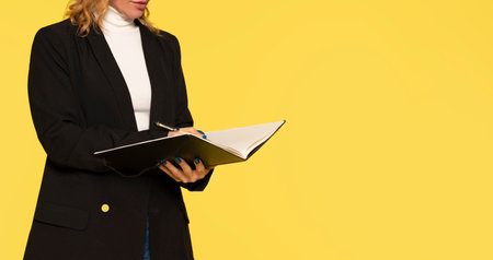 part of body woman with pen writing to folder on yellow backgroundの写真素材