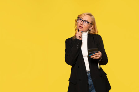 woman with hand on cheek thinking on yellow background with copy spaceの写真素材